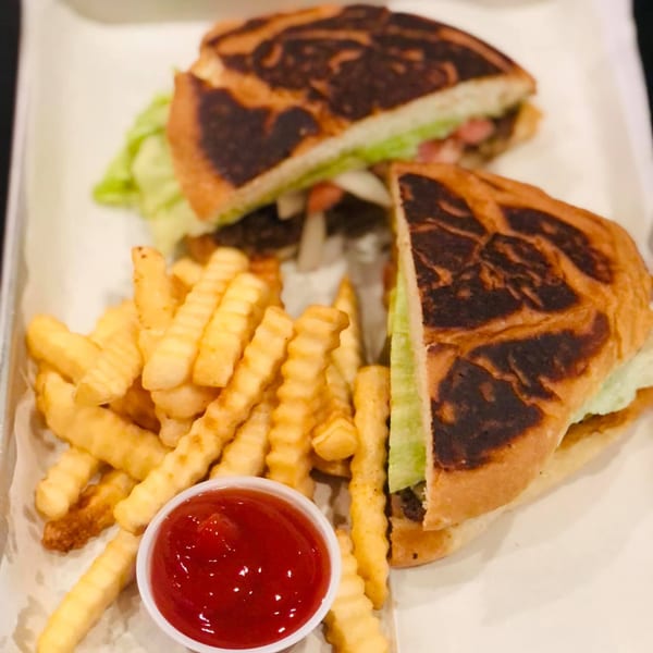 Two halves of a Mexican torta sandwich with lettuce, served with crinkle-cut fries and ketchup.