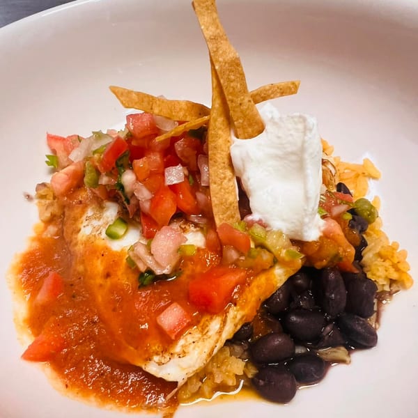 Mexican dish with fried egg, salsa, black beans, rice, sour cream, and tortilla strips.